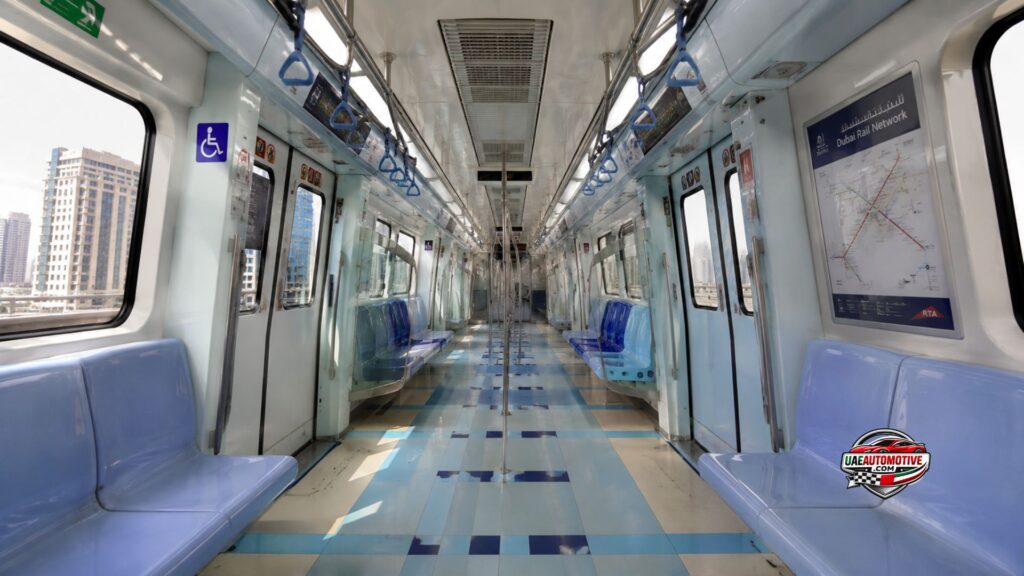 Interior view of a modern Dubai Metro train with clean blue seating, overhead handrails, bright lighting, route maps, and large windows showing Dubai city buildings in a realistic 16:9 scene.