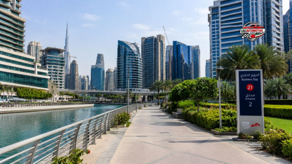 Wide-angle realistic view of Business Bay waterfront in Dubai with modern skyscrapers, canal walkway, palm trees, and Business Bay Metro Station Exit 2 sign during daytime.