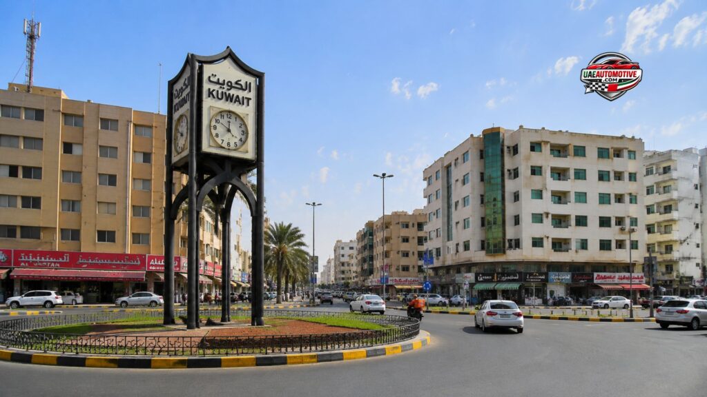 Kuwait Square clock tower in Al Yarmook Sharjah surrounded by residential buildings, local shops, palm trees, and traffic, showcasing a busy central neighborhood scene on a sunny day.